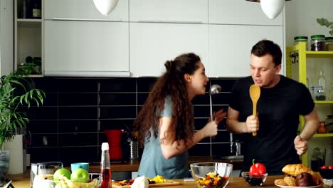 young joyful couple have fun dancing and singing while set the table for breakfast in the kitchen at home