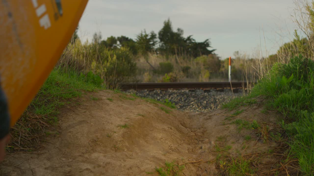 Un surfista trasporta la sua tavola mentre scende a piedi verso uno spot per il surf remoto in una zona costiera.