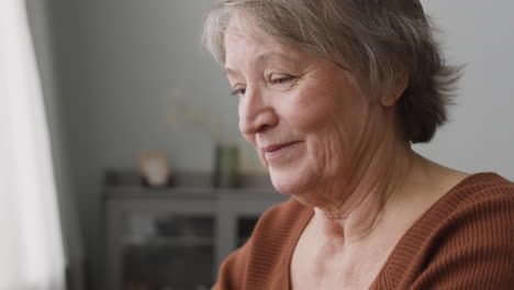 Glückliche-Seniorin,-Die-Zu-Hause-Am-Schreibtisch-Sitzt,-Während-Sie-Einen-Laptop-Benutzt