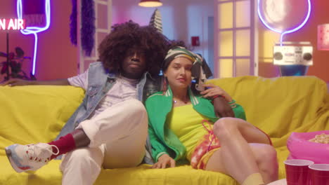 couple posing on a yellow sofa in a neon-lit room