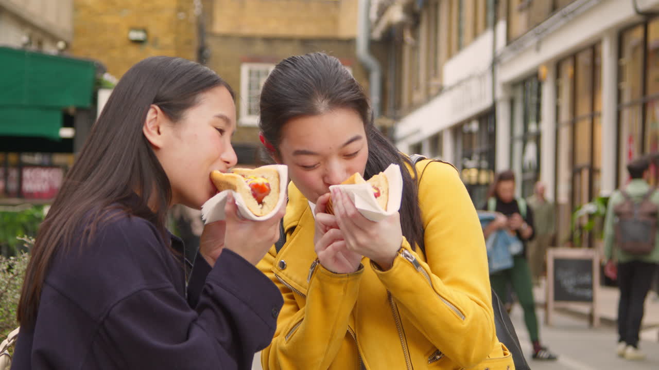 길거리 음식 시장에서 구입한 핫도그를 먹는 두 명의 젊은 여성 친구 1