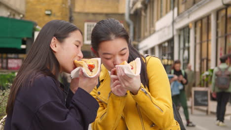 Zwei-Junge-Freundinnen-Essen-Hot-Dogs,-Die-Am-Straßenmarktstand-Gekauft-Wurden-1