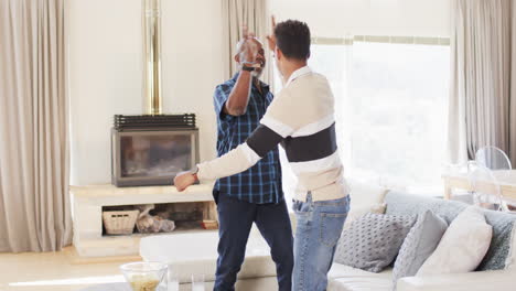 excited african american father and adult son cheering at sport on tv and high fiving, slow motion