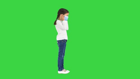 little girl taking her face mask off and smiling at camera on a green screen, chroma key