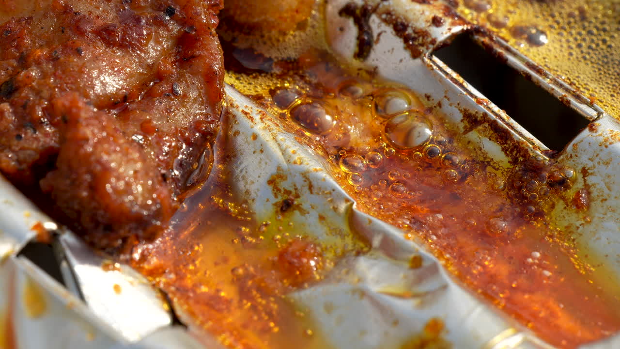 Grasso che sfrigola e ribolle dalla carne su un vassoio di alluminio