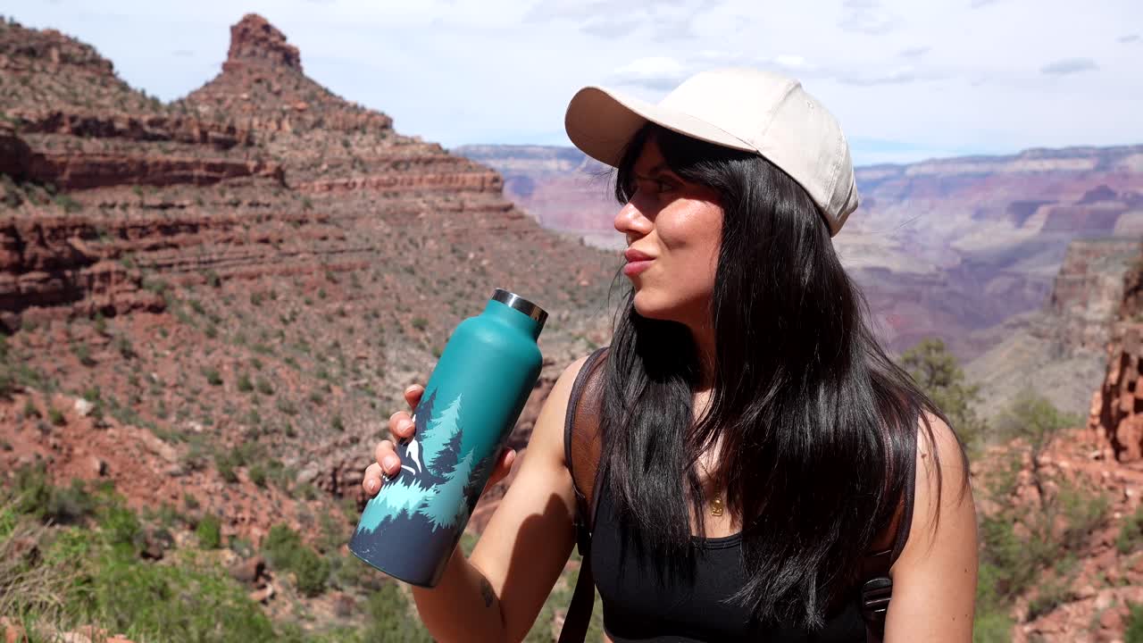 Giovane donna che beve acqua dalla bottiglia durante un'escursione in un canyon desertico