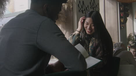 multi ethnic couple watch menu and talk multi ethnic couple sit at the table near window watch menu and talk african american man and asian woman on a date in cafe diverse guests in restaurant with modern design public eating concept