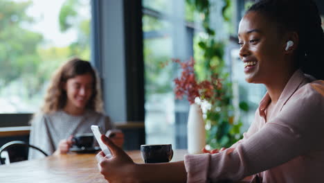 Joven-Empresaria-Con-Auriculares-Inalámbricos-Haciendo-Videollamadas-Por-Teléfono-Móvil-En-Una-Cafetería