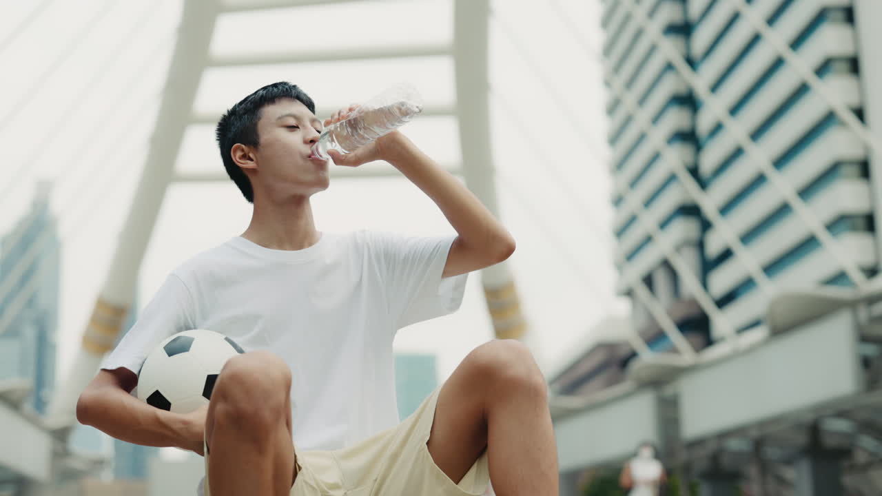 Man drinking water with soccer ball in city
