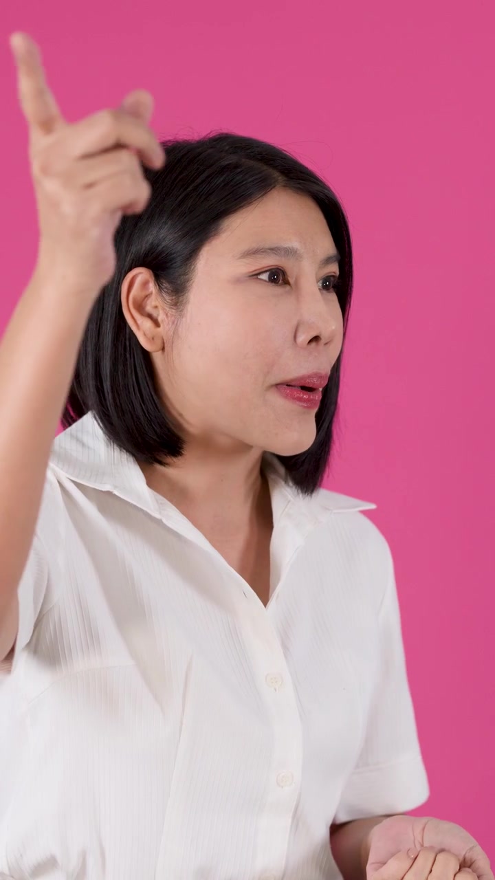 ภาพระยะปานกลางของหญิงชาวเอเชียกำลังพูดคุยและใช้ท่าทางมือที่สื่ออารมณ์โดยมีพื้นหลังสีชมพู