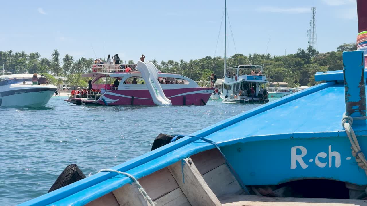 A vibrant yacht with a slide hosts a lively gathering in sunny Phuket, surrounded by clear blue waters and lush greenery