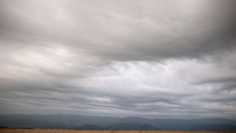 Dramatic-grey-and-white-textured-clouds-spread-across-grassy-plains,-pan-down