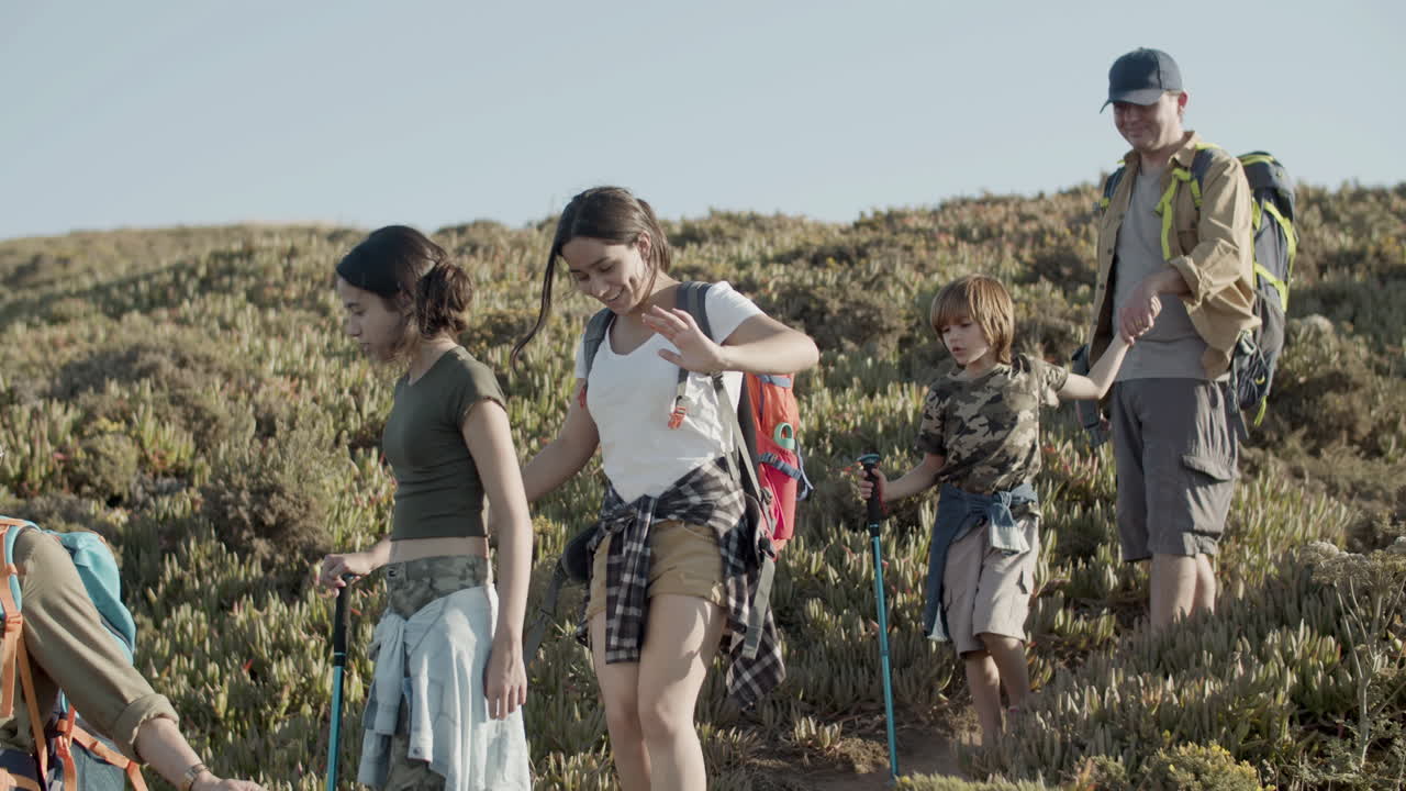 feliz familia caucásica bajando una pendiente empinada haciendo senderismo en las montañas