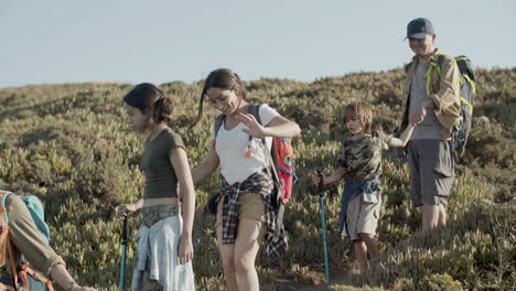 feliz familia caucásica bajando una pendiente empinada haciendo senderismo en las montañas