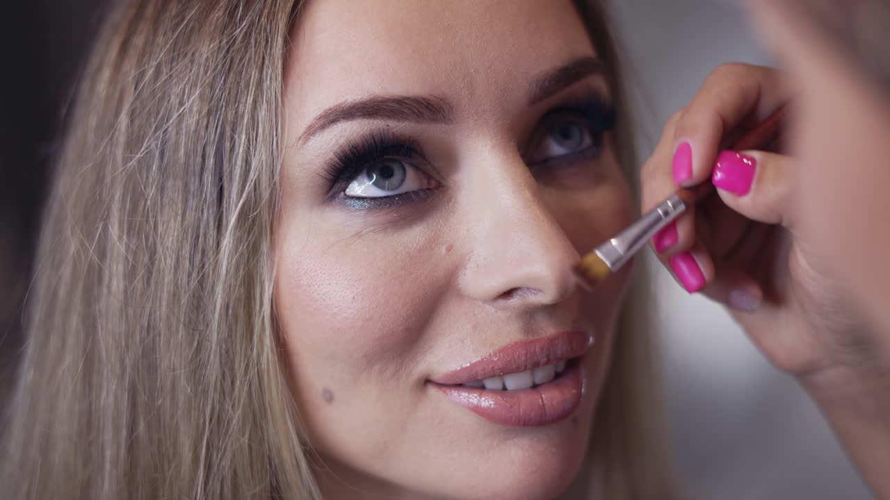 Makeup artist contouring model's nose using a brush