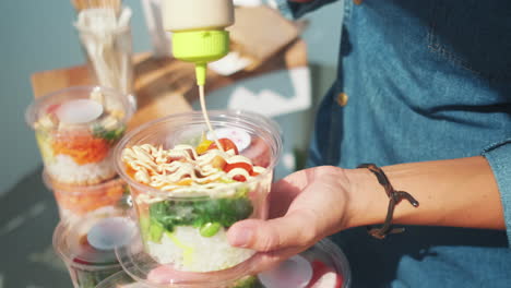 primer plano de la persona que vierte un delicioso aderezo encima de un tazón de poke fresco con diferentes verduras