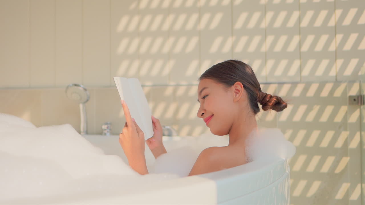 Beautiful young woman relaxes reading a book in bathtub. Slow motion