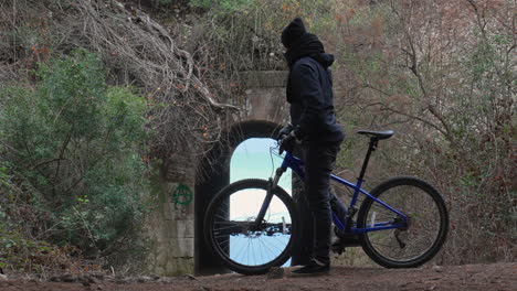 Der-Radfahrer-Hält-An,-Schaut-Durch-Den-Tunnel,-Der-Zum-Meer-Führt,-Und-Fährt-Weiter