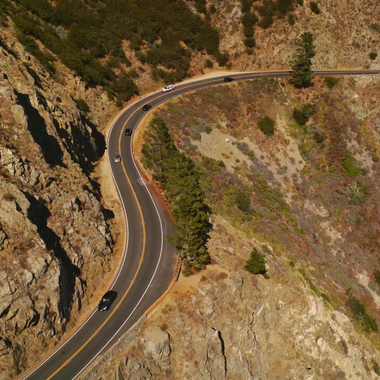 Lively road with cars moving back and forth in the mountainous landscape. Huge mountain with little greenery on sunny day from aerial view