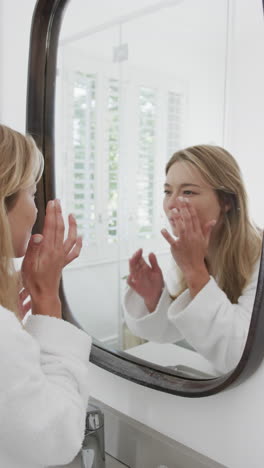 vertical video of biracial woman touching face looking in mirror in bathroom, slow motion
