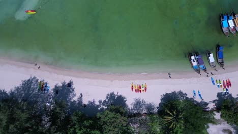 Koh-Phi-Phi-Bay,-colorful-traditional-longtail-boats-are-floating-on-calm-turquoise-water