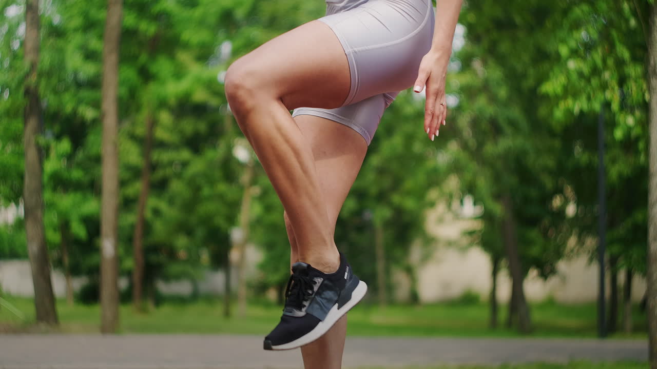 한 젊은 여성이 공원에서 여름에 스포츠 의류를 입고 벤치에 뛰어다니고 있습니다. 육상 백인 여성이 공원에서 훈련합니다.