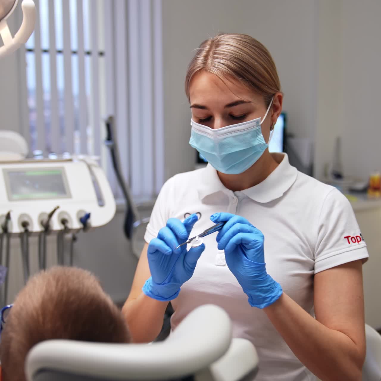 Young beautiful female dentist taking a metal instrument. Doctor is starting dental examination of a little boy. Nurse sitting on the other side of a patient