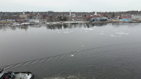 Close-up-aerial-footage-of-flying-over-small-tugboat-pulling-barge,-forward-flight-over-to-town-of-Bath-ME