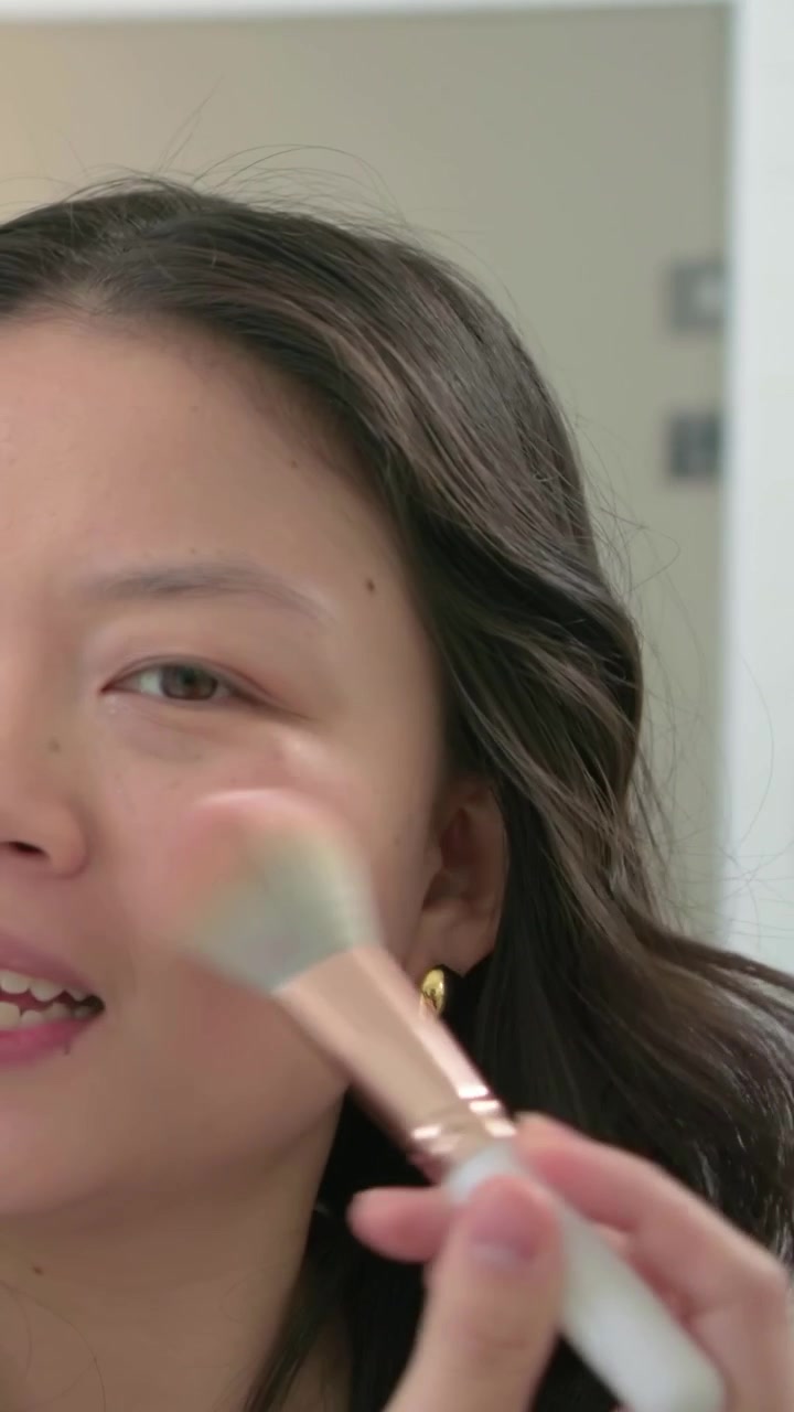 Vertical video: Looking at mirror woman blending blush with fluffy brush at vanity for even cheeks