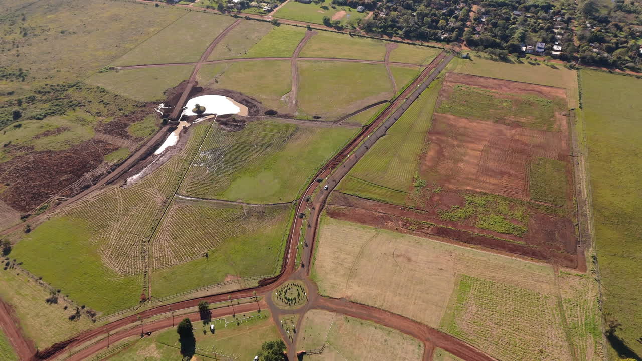 High aerial of car driving on rural dirt road through green countryside