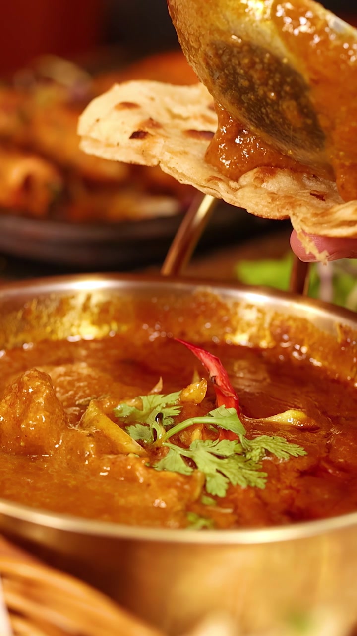 Primo piano di densa salsa al curry versata su pane piatto in un'ambientazione tradizionale di un ristorante indiano a Bangkok.