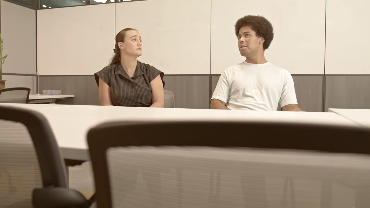 20대 아프리카계 미국인 남성과 20대 백인 여성이 오른쪽에서 왼쪽으로 이동하는 비디오와 함께 비즈니스 미팅에서 이야기하고 있습니다.