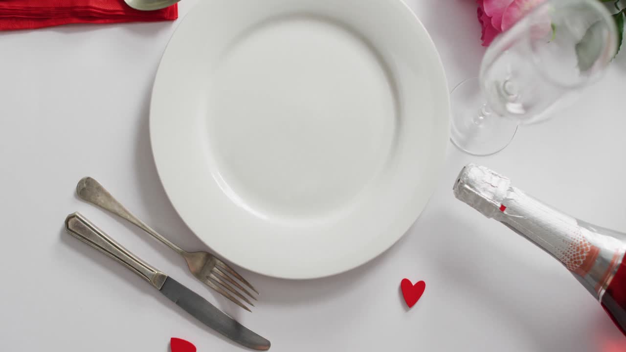 Champagne and plate with cutlery on white background at valentine's day