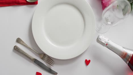 champagne and plate with cutlery on white background at valentine's day