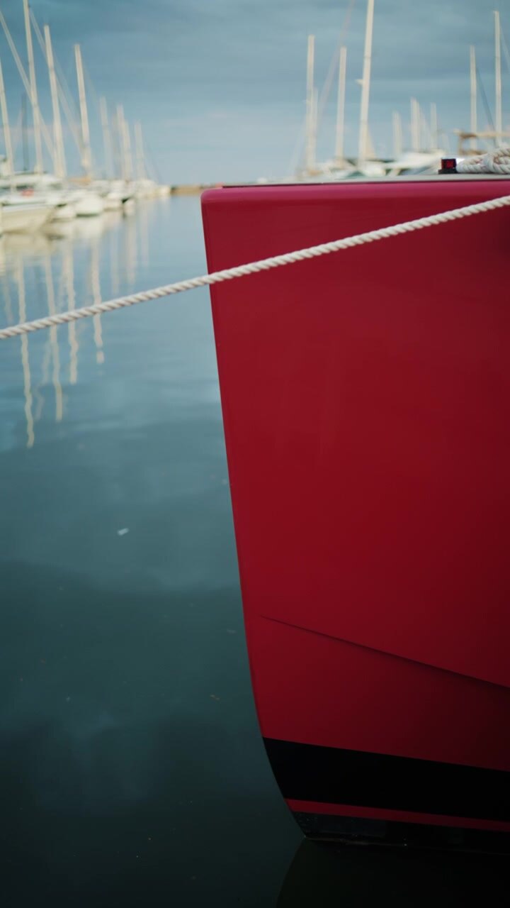 Primo piano dello scafo rosso di uno yacht e di una cima d'ormeggio riflessi nell'acqua calma del porto turistico di Port Vauban.