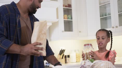 padre y hija biraciales felices desempaquetando las compras en la cocina, cámara lenta