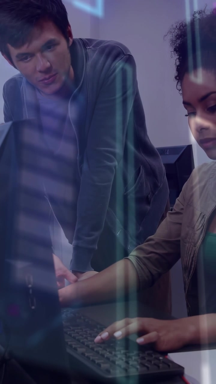 Woman starting typing, man leaning over monitor guiding trainee in tech lab with light streaks