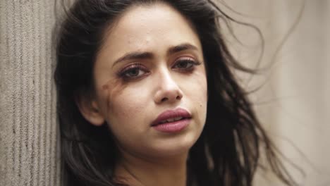 Close-up-headshot-of-a-young-indian-female-with-smudged-make-up-sad-by-the-wall-slowmotion