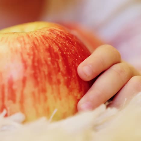 the baby's hand holds a large red apple that lies on the floor