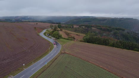 Red-car-drives-on-countryside-road-at-Luxembourg-on-cloudy-day,-aerial
