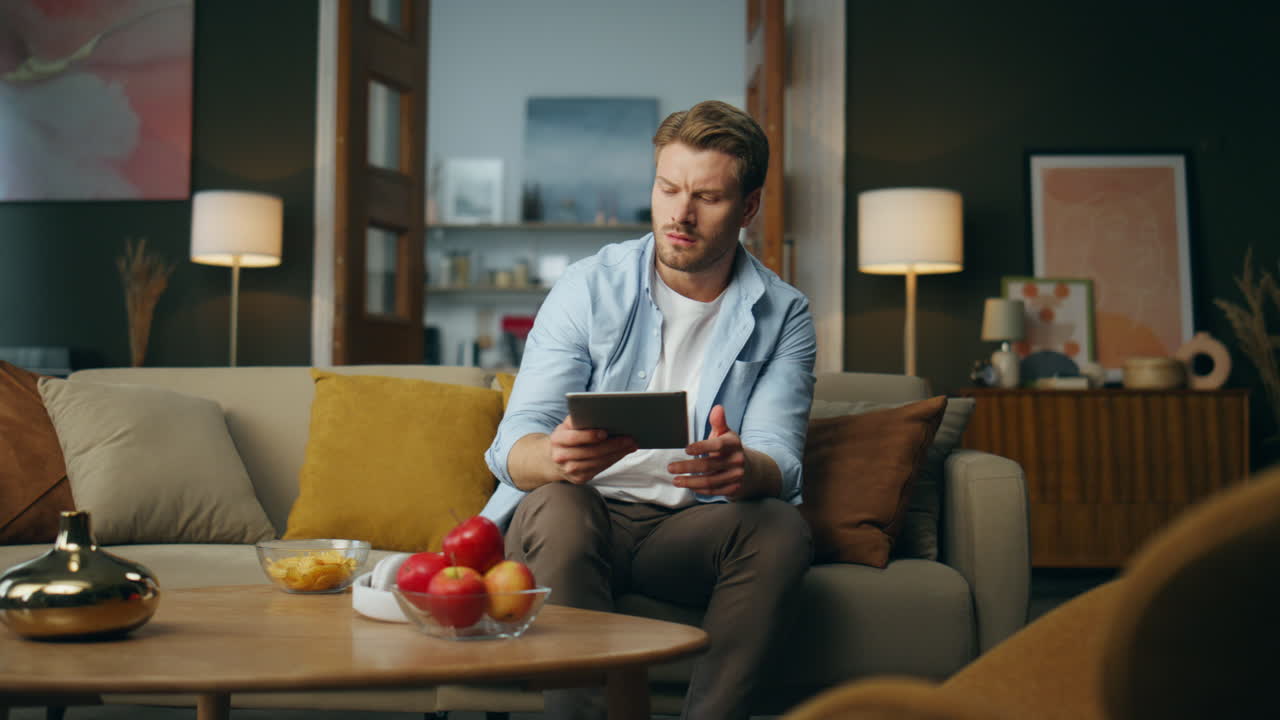 Thoughtful man putting tablet table at home. Pondering guy finding solution