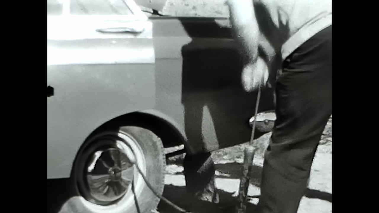 Man Standing Next to Car in Old Black and White Video From the Soviet Union Archive. CIRCA USSR 1970: An intriguing black and white video capturing a man standing next to a classic car, preserved in the Soviet Unions archive.