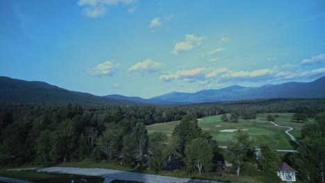 a wide angle panning shot of the white mountains in new hampshire as they sit beyond a forest and gold course