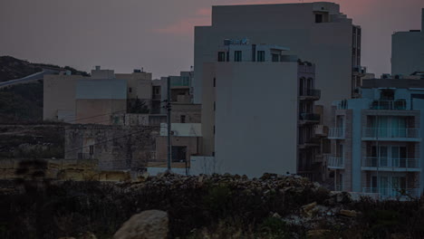 setting sun drops below clouds into darkness on concrete buildings, timelapse