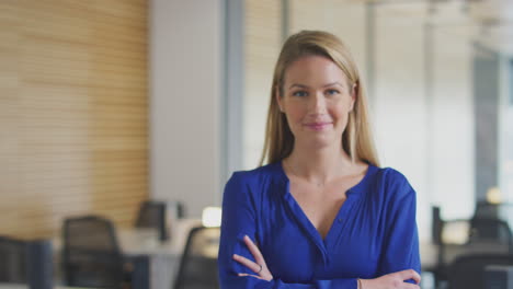 portrait of smiling young businesswoman walking into focus in modern open plan office