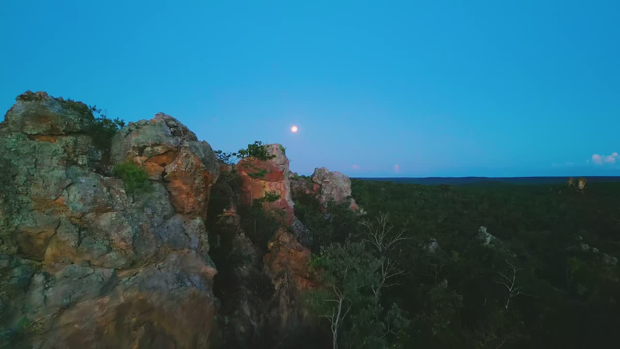 Capturing the Pedra do Gaviao Natural Reserve in Cavalcante, Goias, Brazil, with moon rising over the horizon, illuminating the rocky landscape and lush vegetation at twilight, drone establishing shot