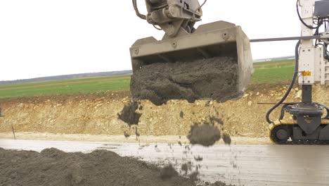 Excavator-bucket-unloads-fresh-concrete-onto-first-layer-of-concrete-road-surface