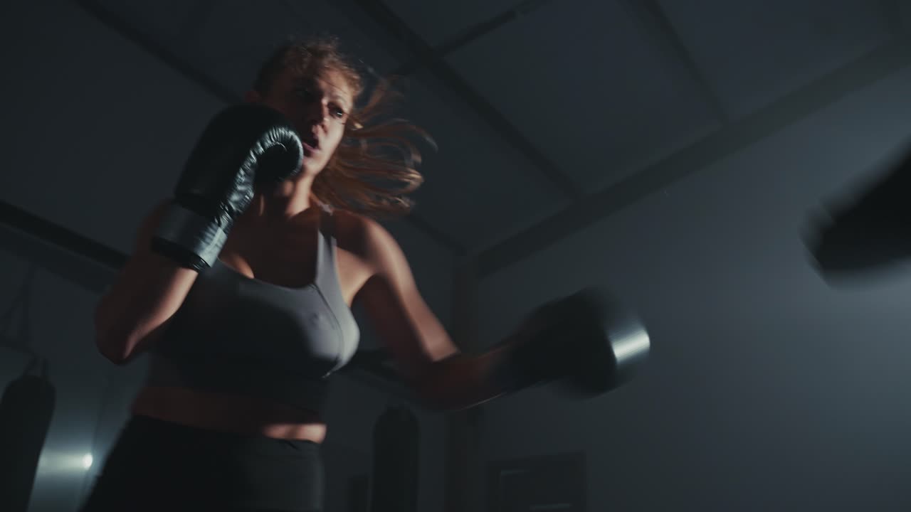Boxeadora entrenando con manoplas de foco en un gimnasio oscuro