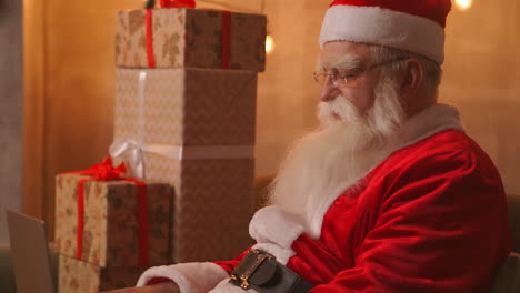 Santa-Claus-is-working-on-a-laptop-sitting-at-home-on-the-sofa-in-the-background-of-Christmas.-Santa-responds-to-children-emails.-High-quality-4k-footage