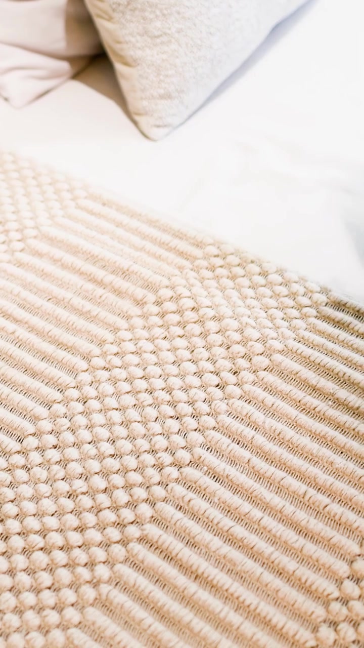 Una persona posiziona con cura un tappeto intrecciato beige e texturizzato su un divano bianco all'interno.